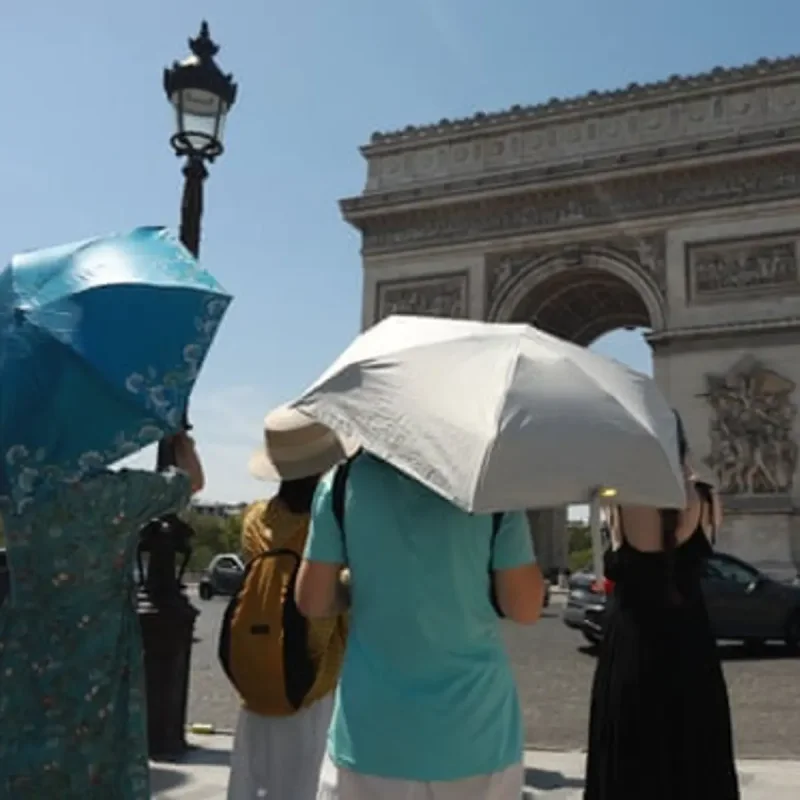 People walking through a sunlit European city street during a summer heatwave